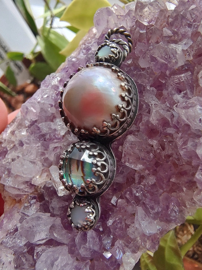Close up view of a sterling pendant with pink pearl and abalone, sitting on an amethyst crystal.