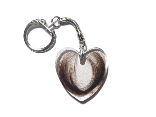 A flat, heart shaped key chain encasing a loved ones hair. 