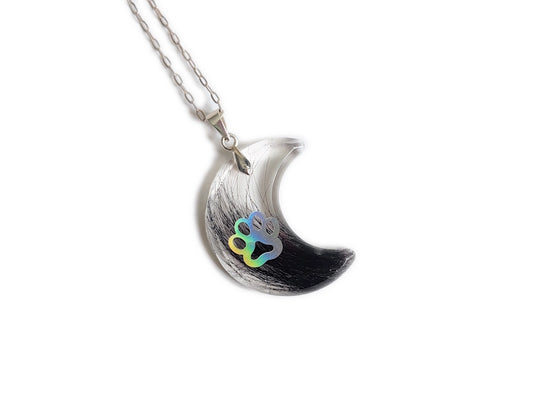 A moon shaped pendant with pet fur and paw print, on a silver chain over a white background.