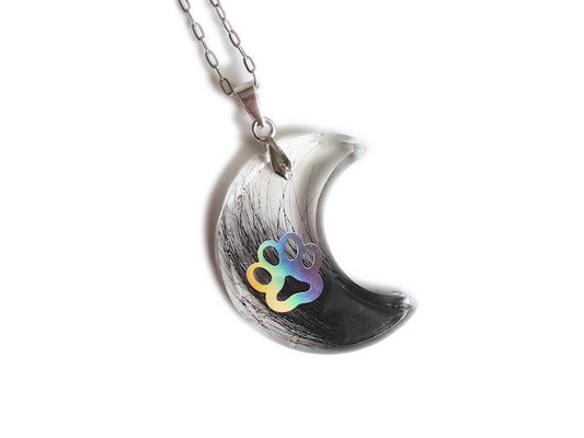 A moon shaped pendant with pet fur and paw print, on a silver chain over a white background.