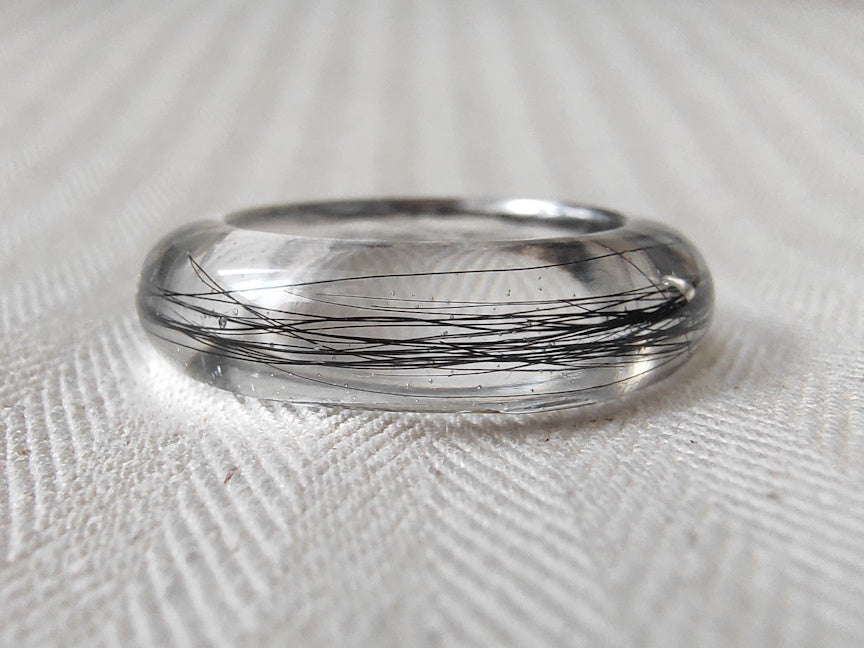 Close up view of a clear resin keepsake ring with black hair.