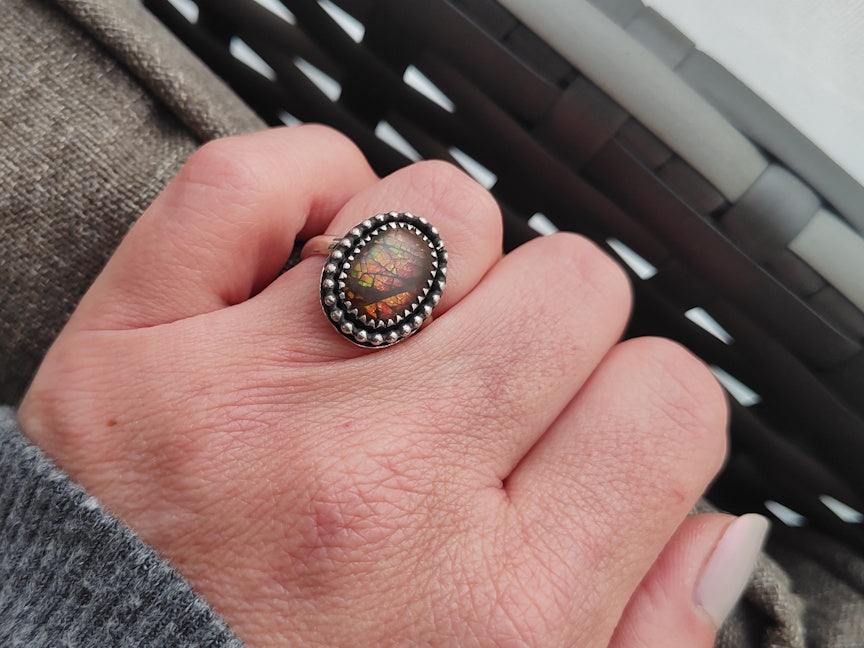 Hand wearing a ring with a colorful ammolite stone against a blurred background