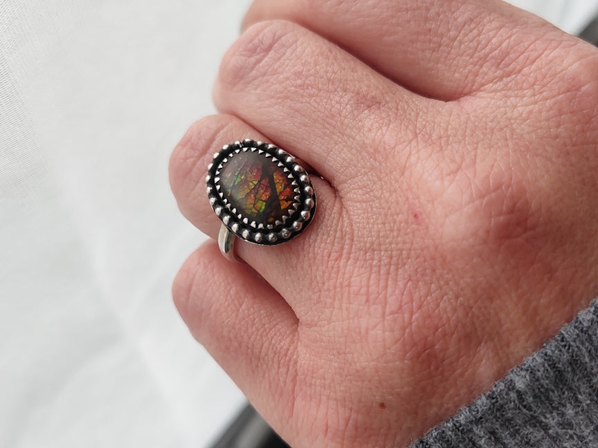 Close-up of a hand wearing a ring with a colorful ammolite gem on a white background