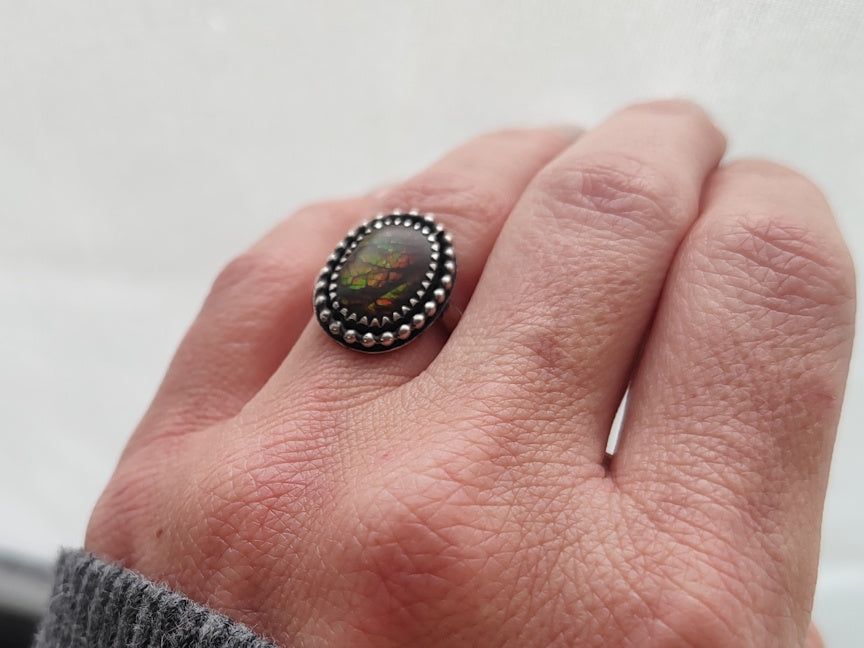 Hand wearing a ring with an ammolite stone on a light background