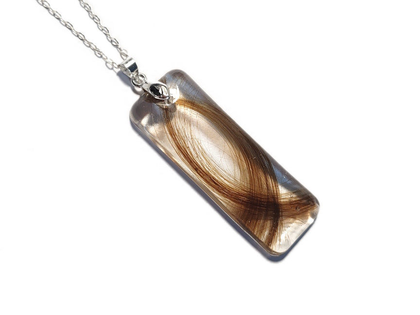 A bar shaped pendant in clear resin with dark blonde hair.