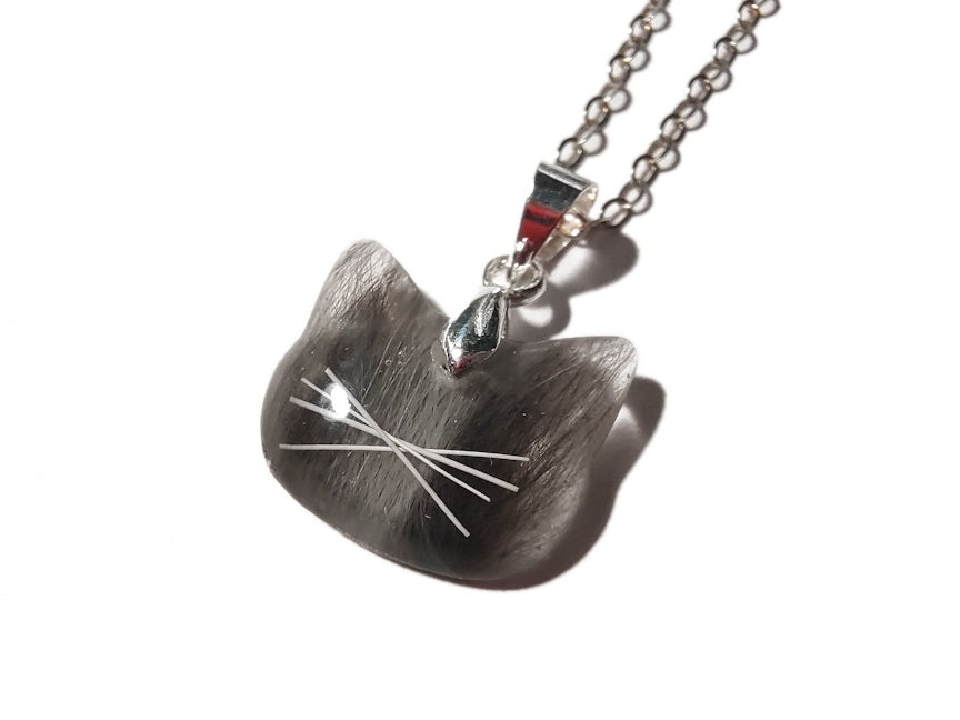 A cat shaped pendant containing black and white fur, and tiny whiskers. 