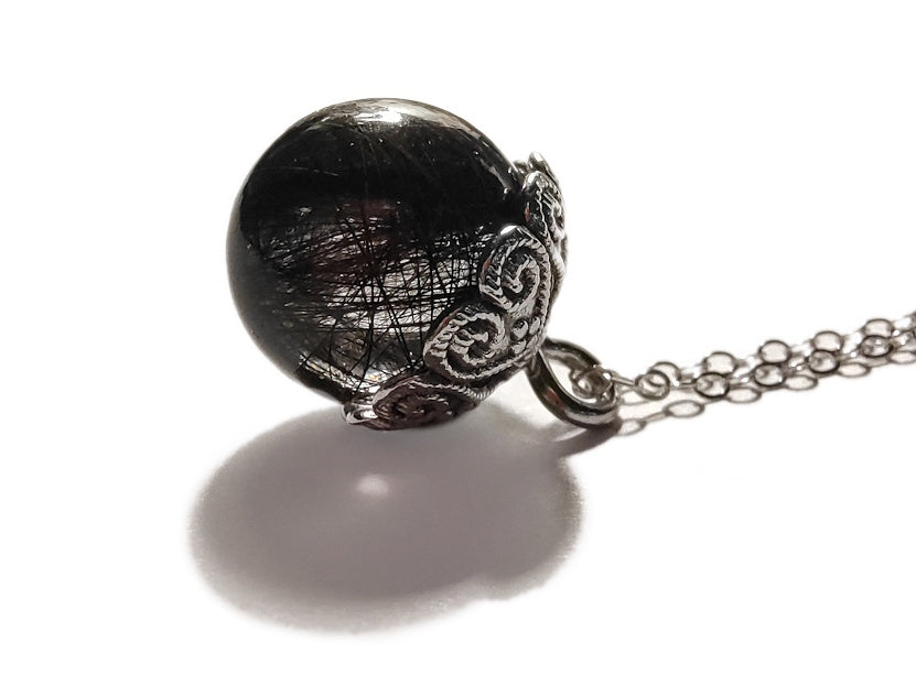 Clear sphere pendant with hair inside, on a chain against a white background