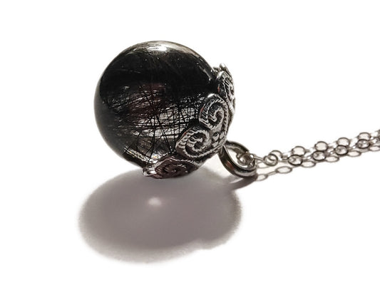 Clear sphere pendant with hair inside, on a chain against a white background