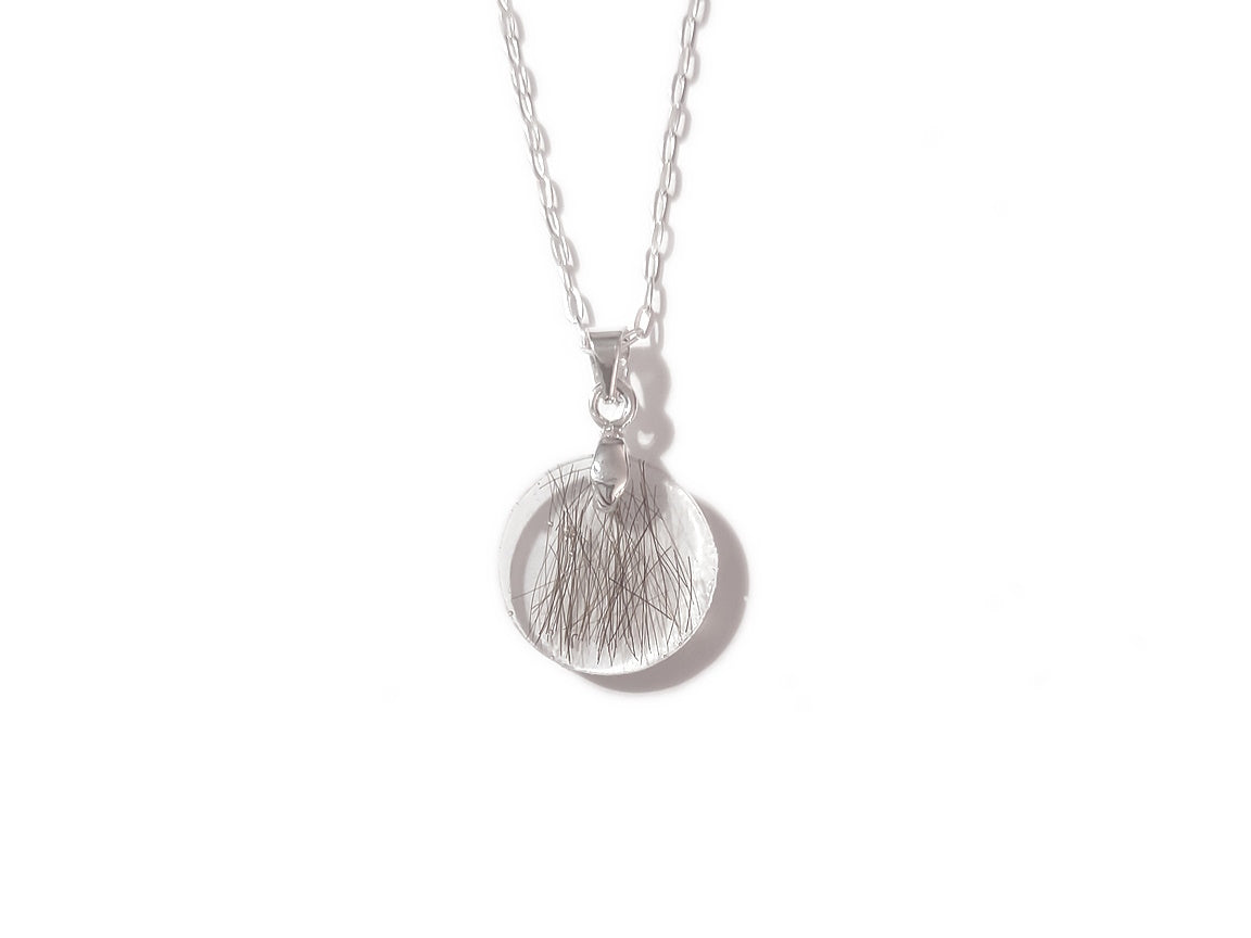 A handmade memorial necklace in the medallion shape, encasing a loved ones hair, fur, or ashes. 