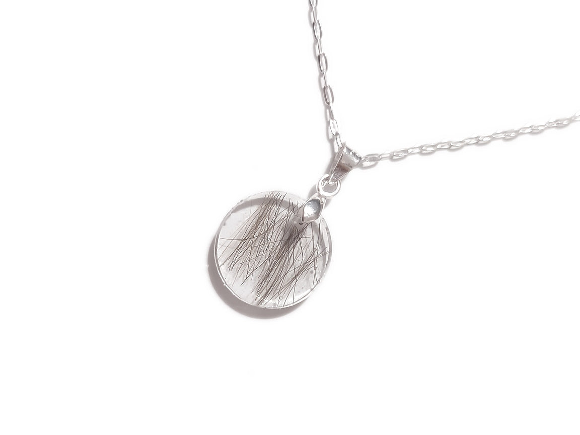 A handmade memorial necklace in the medallion shape, encasing a loved ones hair, fur, or ashes. 