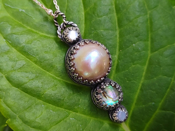 A pendant with pink pearl, abalone and shell on a green leaf