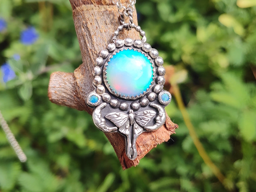 Silver pendant with large manmade opal and a moon and moth motif.