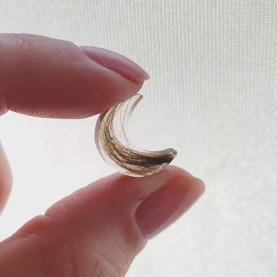 A small moon shaped hair keepsake being rotated between two fingers.