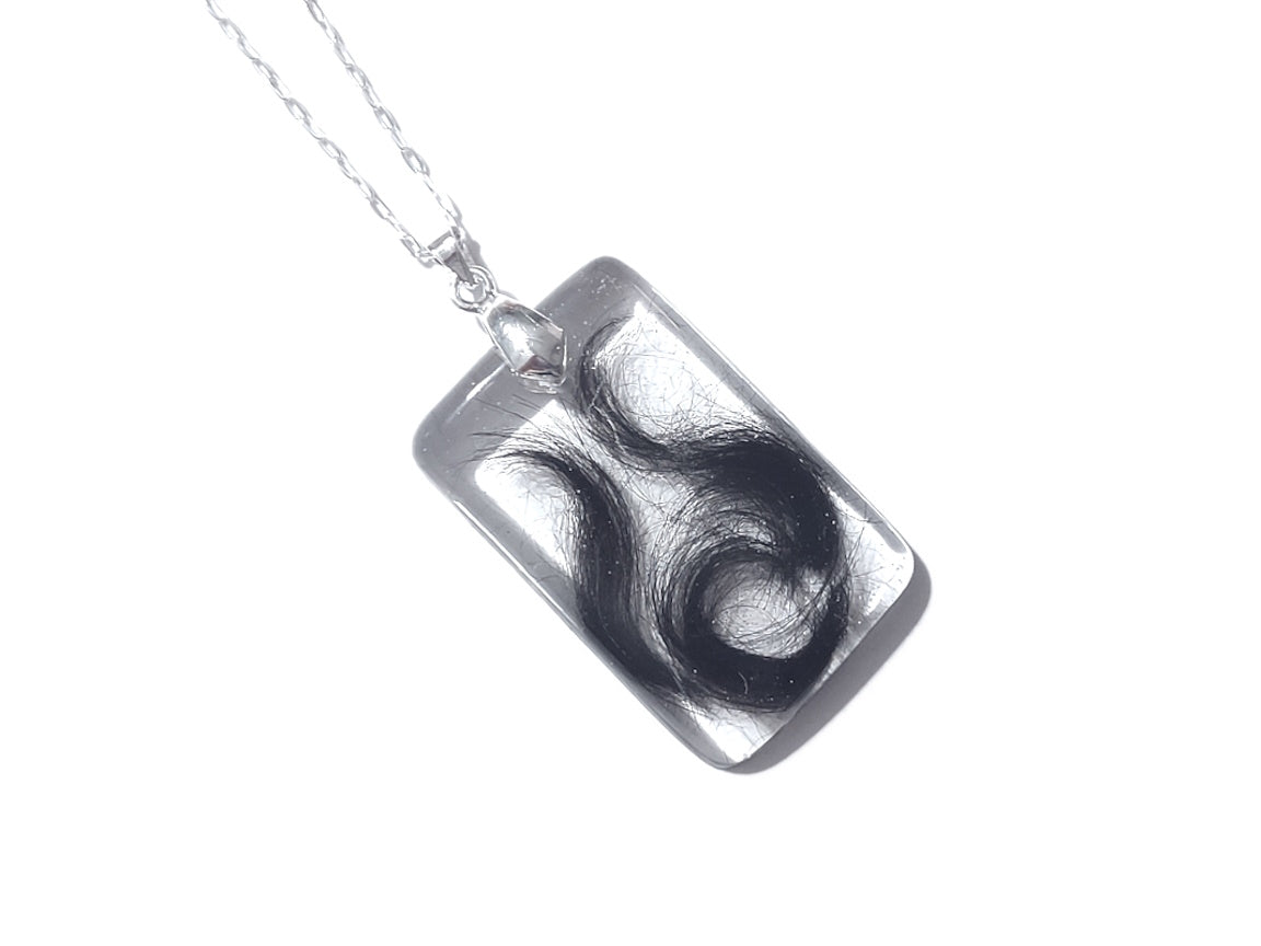 A rectangle shaped keepsake pendant with a small amount of hair inside
