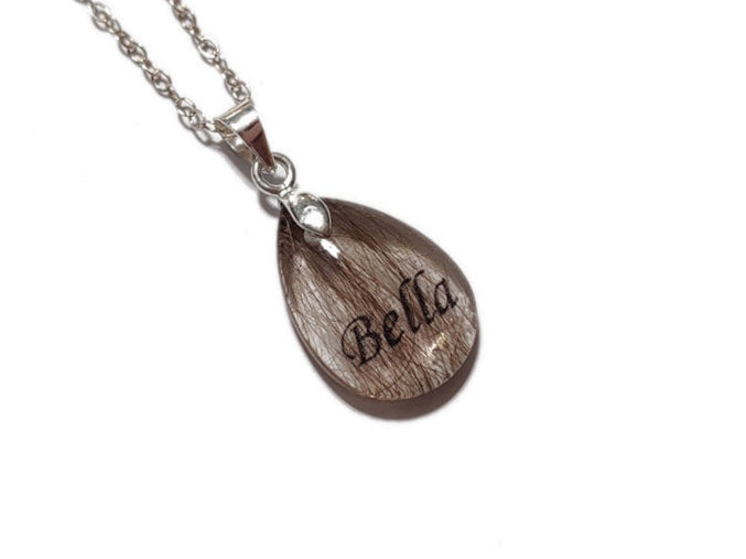 Resin pendant with 'Bella' name and pet fur on a silver chain against a white background