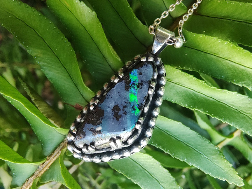 Yowah boulder opal pendant necklace on a chain with a green leafy background.