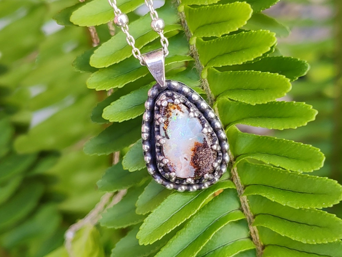 Handmade silver necklace with a pendant featuring a Yowah Boulder  opal stone on green fern leaves.