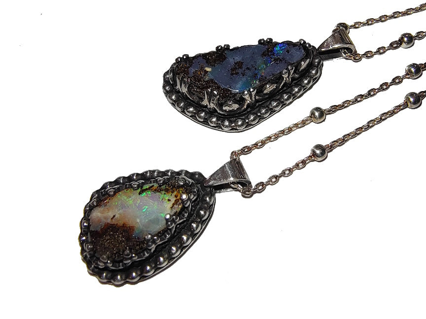 Two boulder opal pendants on silver chains against a white background