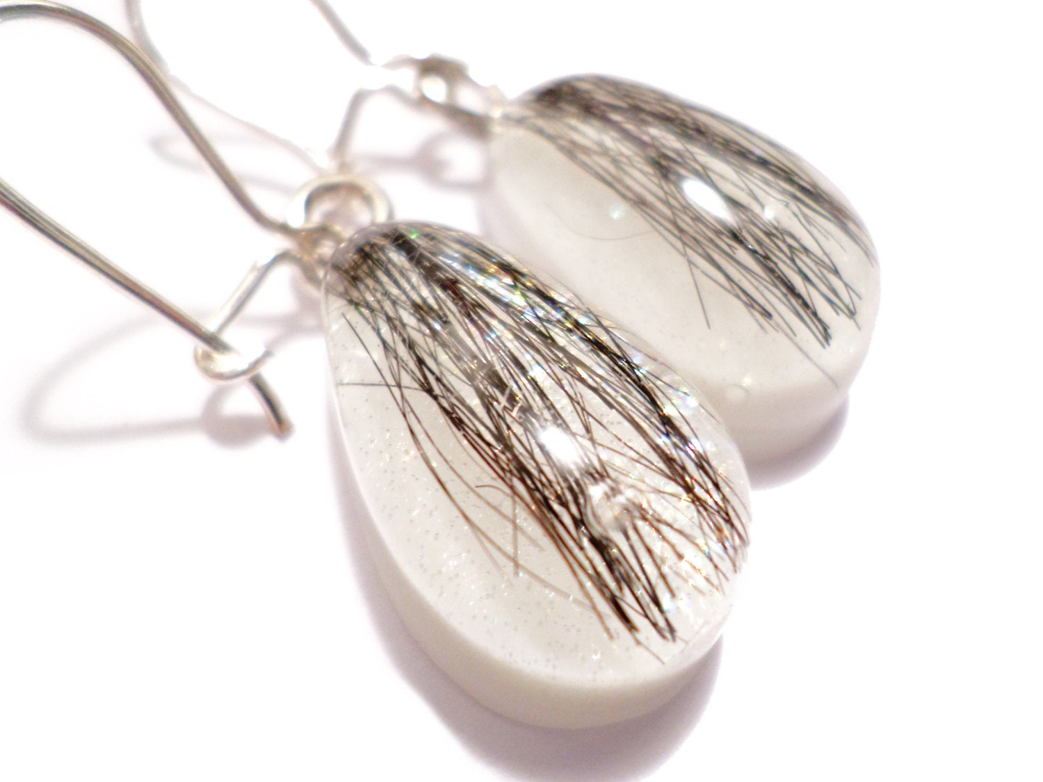 A closeup shot of a pair of teardrop shaped earrings with dark hair and a shimmering pearl backing.