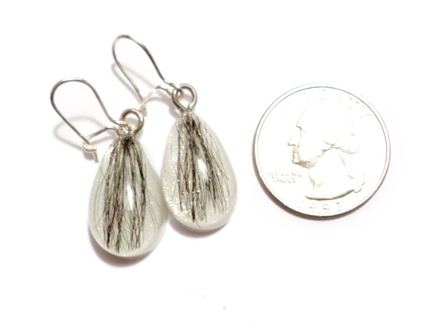 A pair of teardrop shaped earrings with dark hair and a shimmering pearl backing.