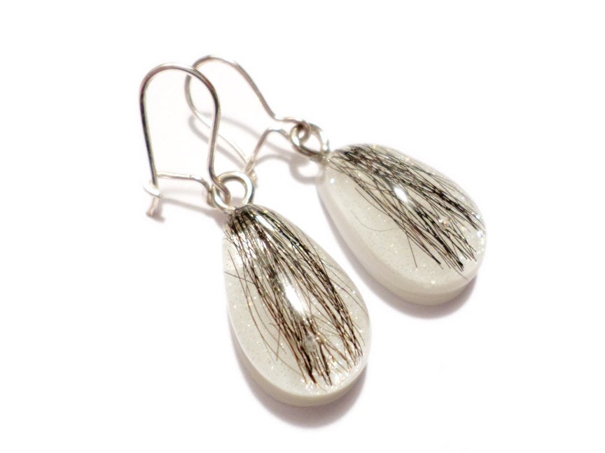 A pair of teardrop shaped earrings with dark hair and a shimmering pearl backing.