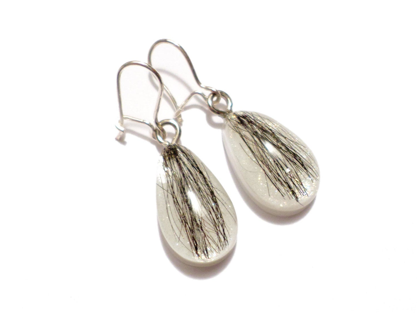 A pair of teardrop shaped earrings with dark hair and a shimmering pearl backing.