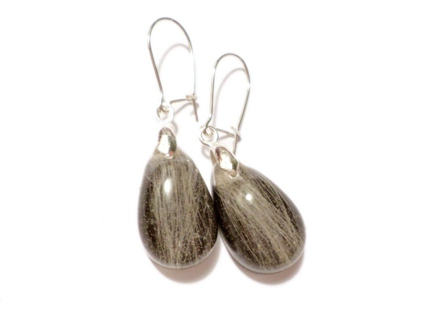 A pair of teardrop shaped earrings with light hair and a black backing.