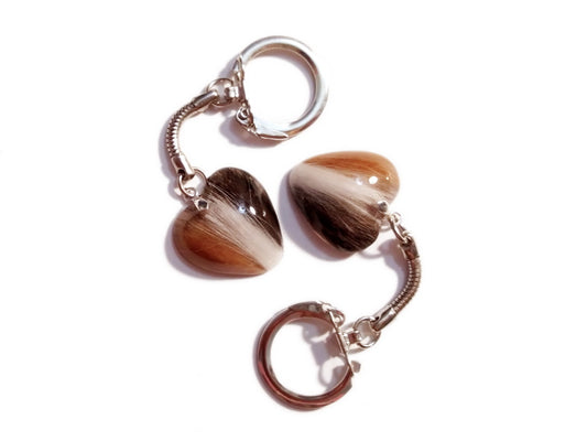 A pair of heart memorial keychains containing calico colored fur